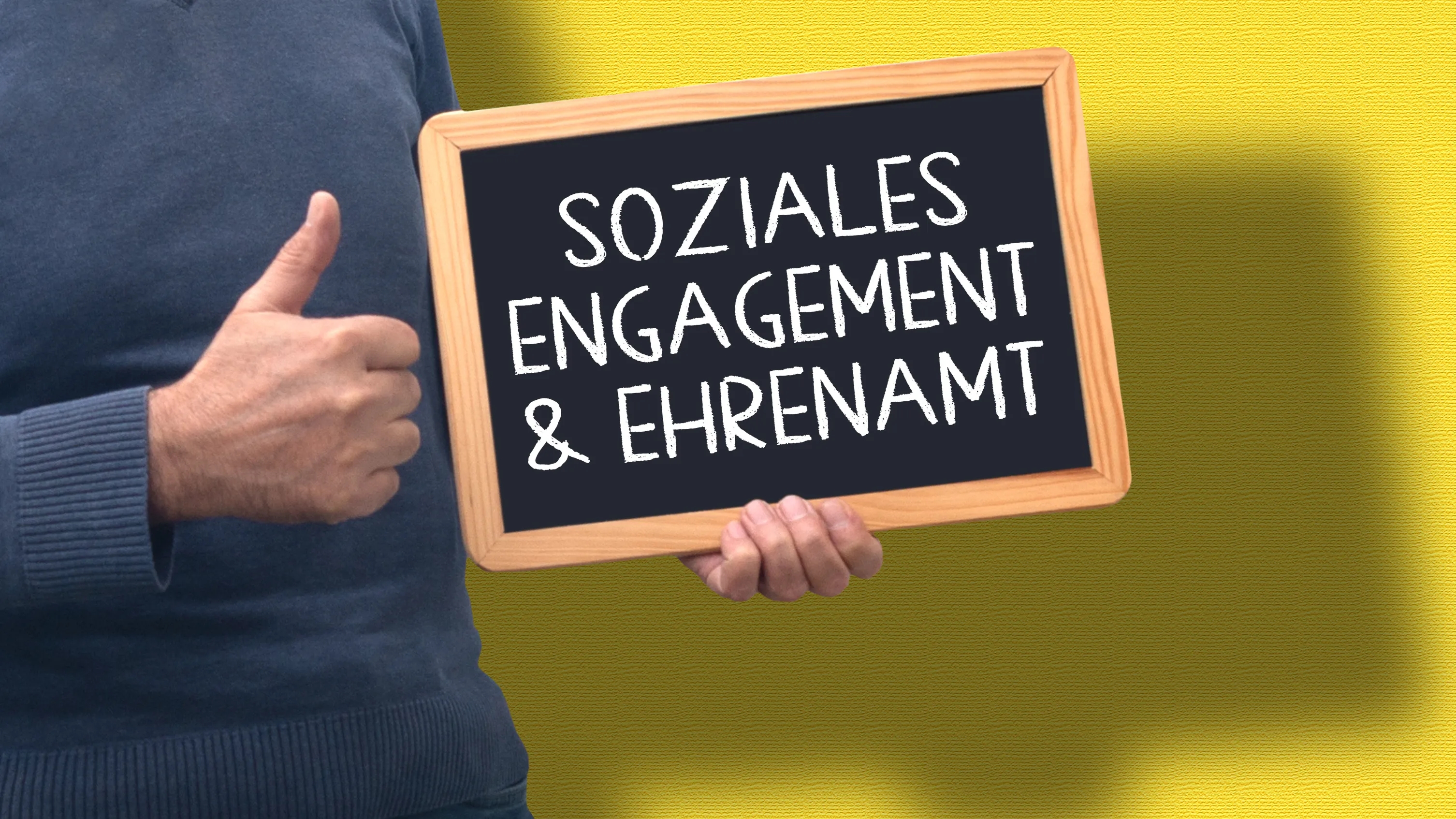 Ein Mann hält ein Schild hoch mit dem Text "Soziales Engagement & Ehrenamt".